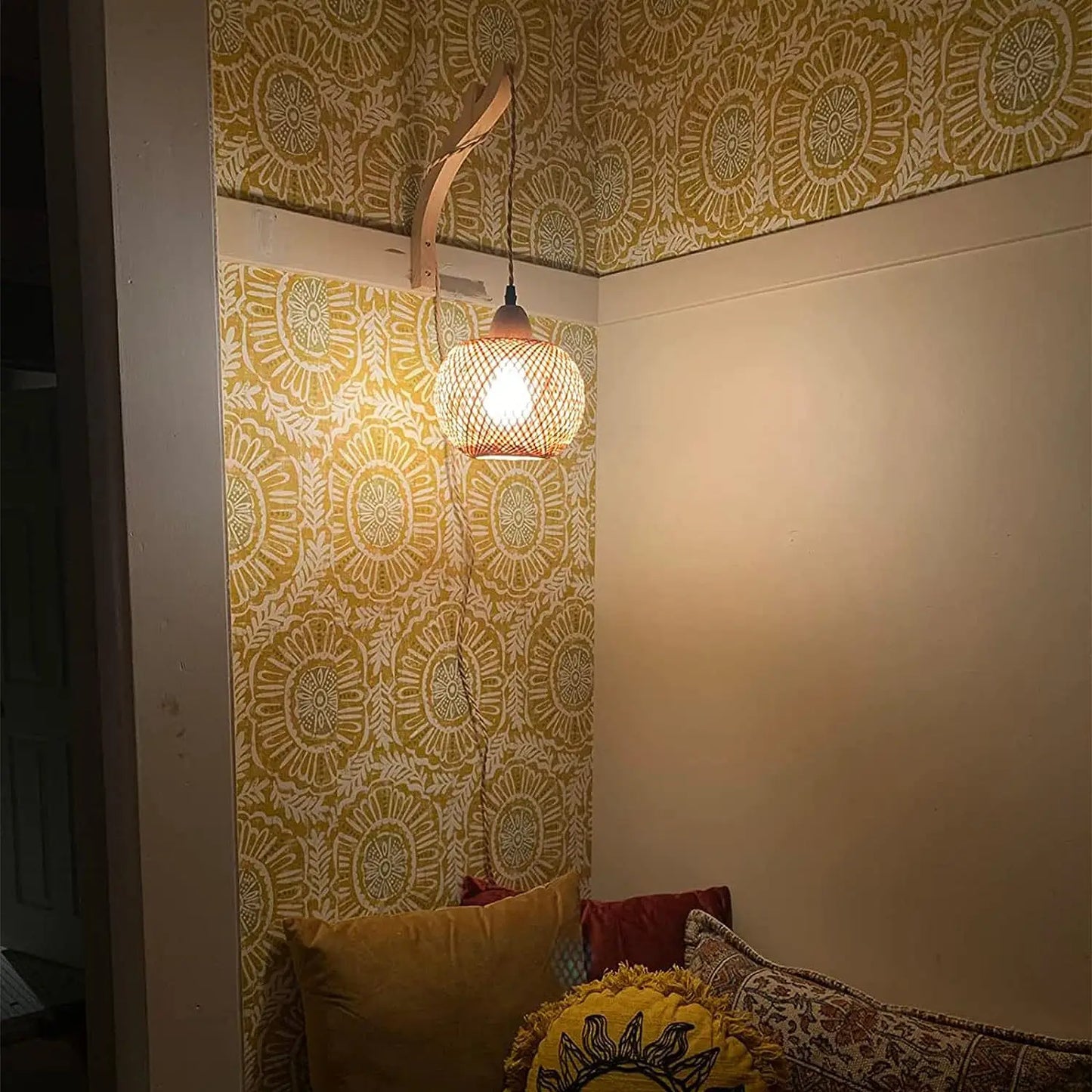 Woven pendant light hanging from patterned yellow and white wallpaper.