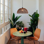 Dining area with a green table, orange chair, wooden chair, and potted plants.