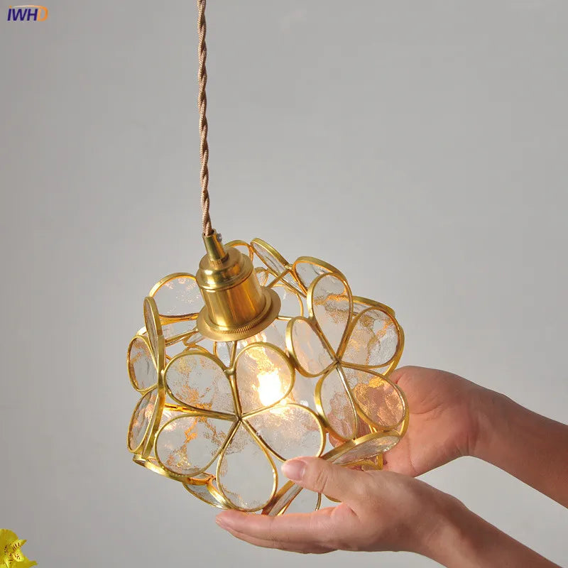 Hand holding a decorative gold pendant light with a geometric design against a gray background.